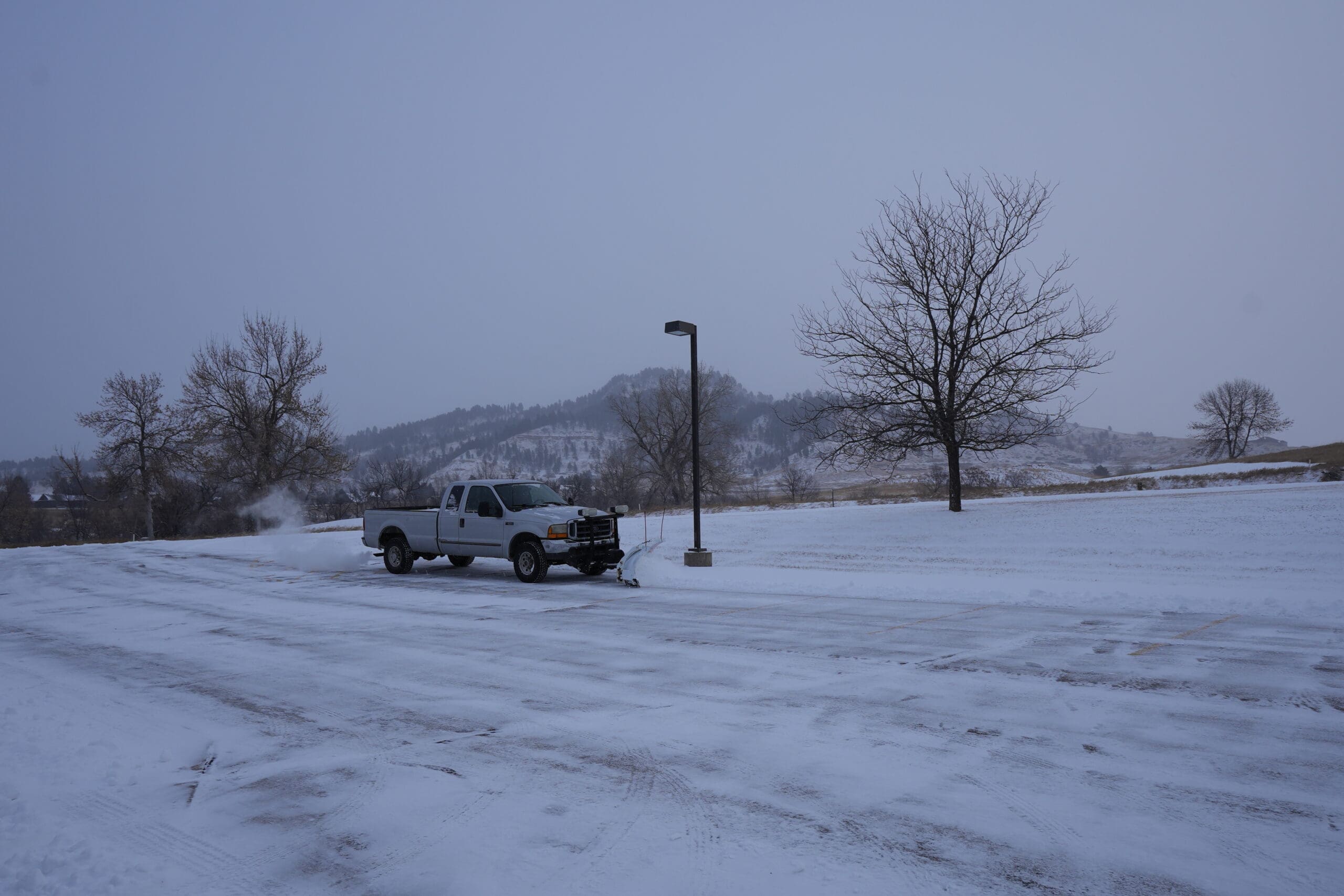 Snow removal truck clearing snow from a commercial parking lot in Spearfish, SD as part of professional snow removal services by South Dakota Services.
